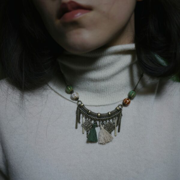 Photographie d'un collier artisanal sur modèle, alliant des perles de céramique, de laiton et des pompons de coton.