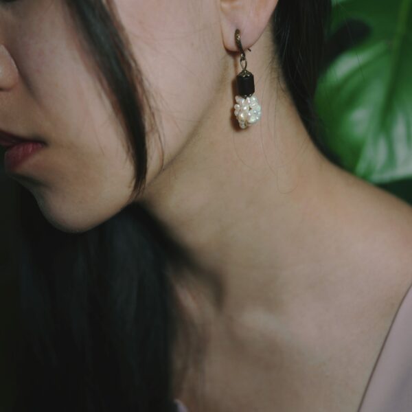 Photo close-up d'un mannequin photo qui porte une boucle d'oreille d'artisan d'inspiration vintage et asiatique faite avec des perles d'eau douce et du bois de rose.