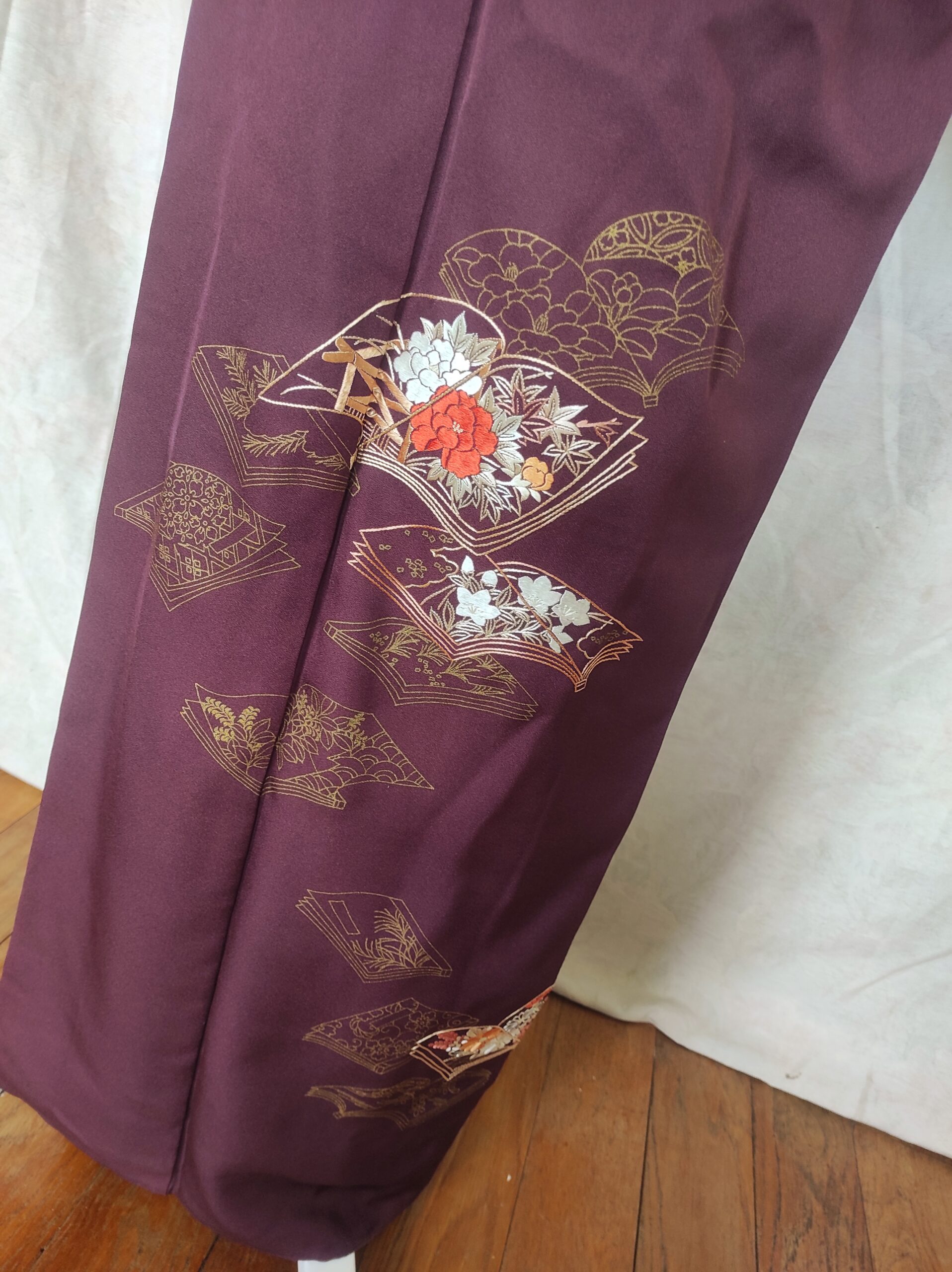 Image du bas du kimono en soie représentant un vol de livres ouverts contenants des fleurs japonaises