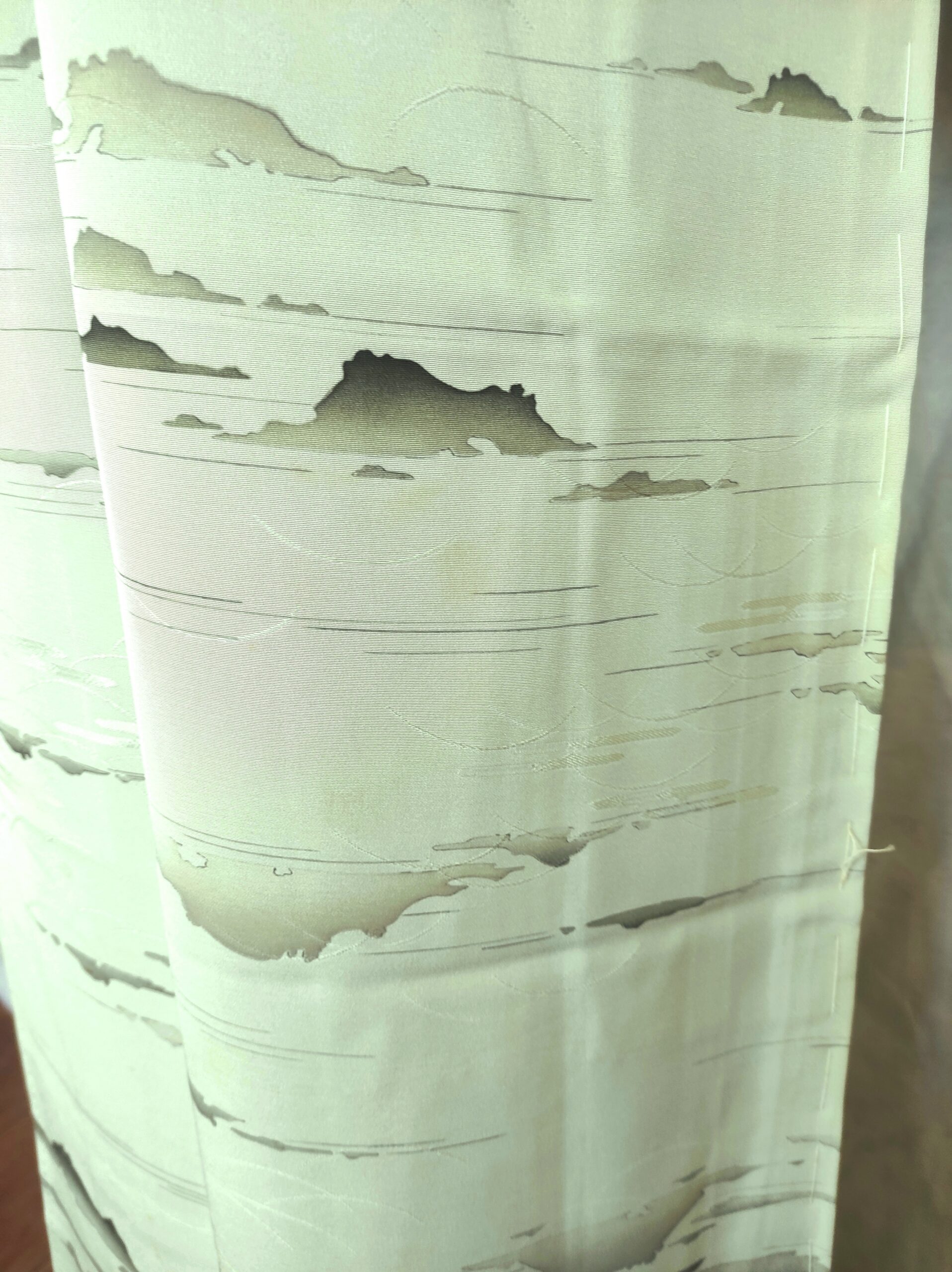 Photo rapprochée d'un pan de kimono de soie vert sur lequel est peint à la main des motifs de montagnes japonaises et de nuages