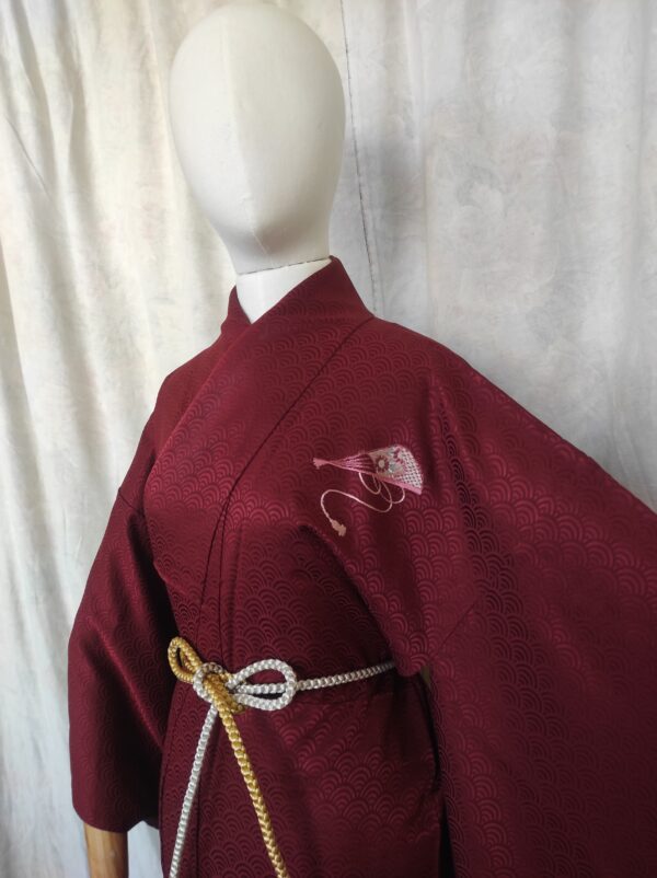 Photographie du haut d'un kimono en soie rouge comporte une broderie en forme d'éventail rose et argenté