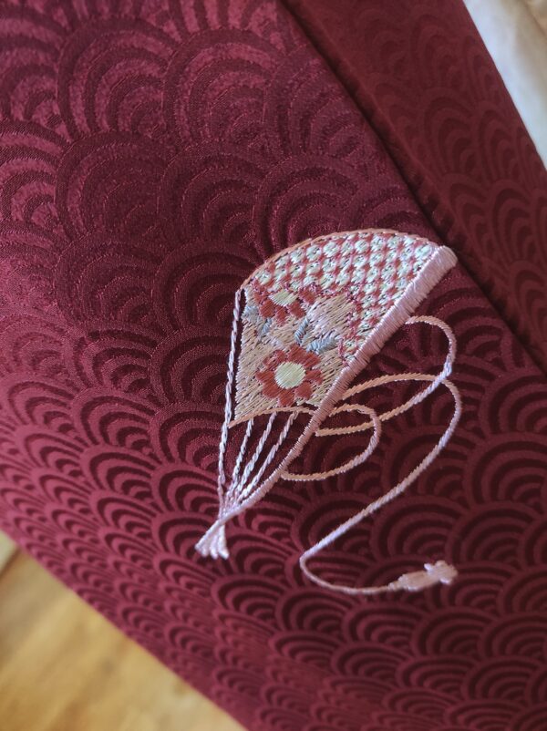 Close-up d'une partie d'un kimono de soie rouge au motif de segaiha comportant une broderie d'un éventail brodé à la main par un artisan