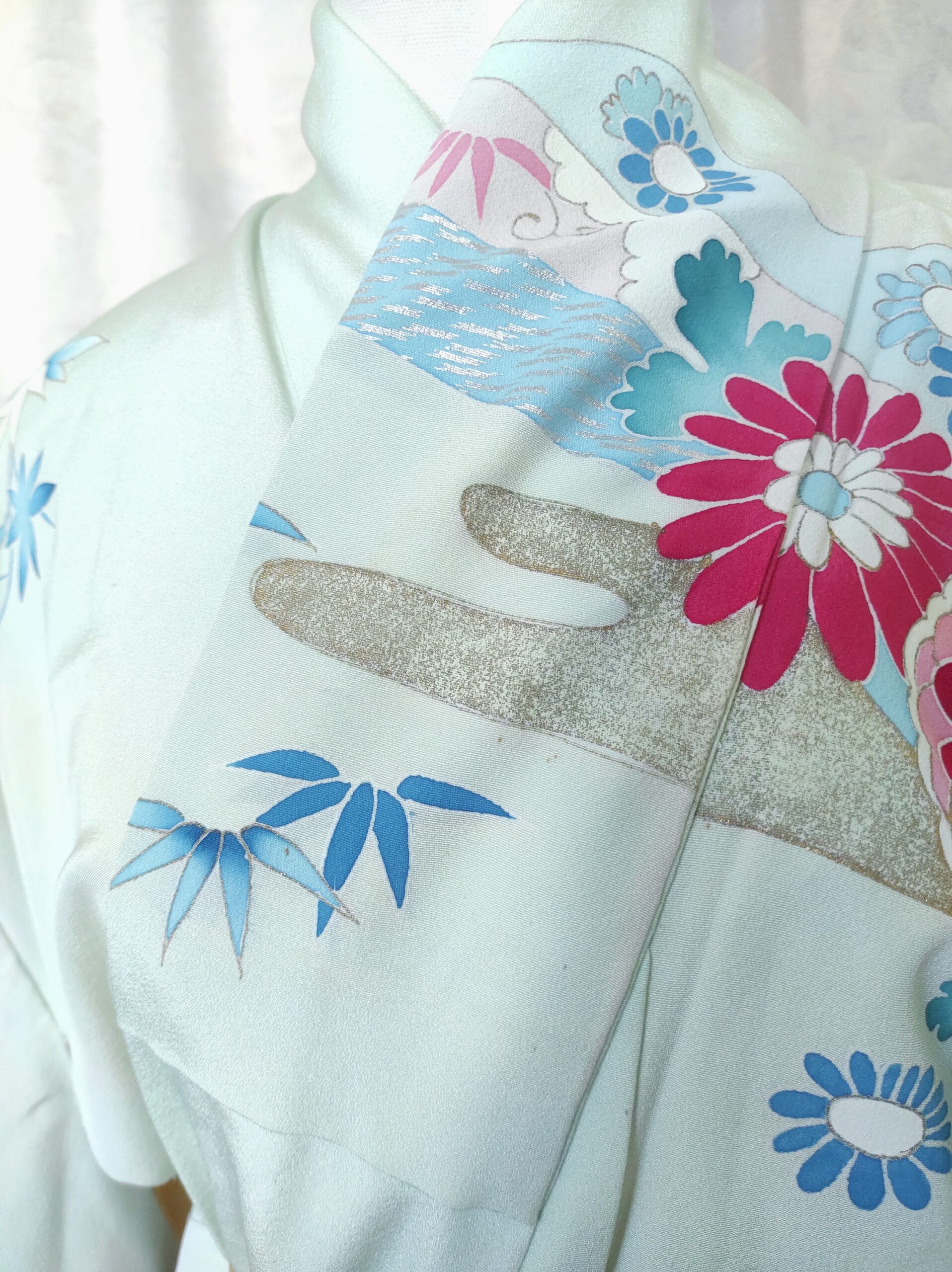 Photographie du col d'un kimono de soie bleu comportant des motifs floraux, des nuages peints à l'or et des feuilles de bambous